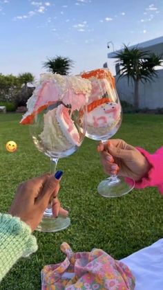 two people toasting wine glasses with food in them on top of the green grass