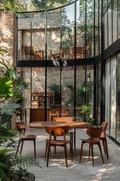 an outdoor dining area with wooden chairs and tables in front of a glass wall that overlooks the trees