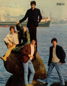 the rolling stones posing on top of a rock in front of a body of water