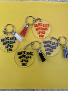 four key chains with different sayings are shown on a yellow background, including one that reads drive safe someone loves you and the other says drive safe someone loves you