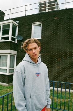 a man standing in front of a brick building Casual College Sweatshirt With Logo Detail, Casual College Sweatshirt With Logo, Streetwear Hoodie With Logo And Relaxed Fit, Logo Detailed Relaxed Fit Hoodie For Streetwear, Relaxed Fit Streetwear Hoodie With Logo, Relaxed Fit Hoodie With Logo For Streetwear, Spring Athleisure Sweatshirt With Embroidered Logo, Sporty Hoodie With Embroidered Logo For Spring, Relaxed Fit Hoodie With Embroidered Logo For Streetwear