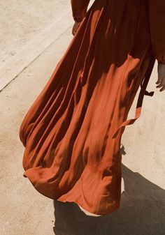 a woman in an orange dress is walking down the street with her hand on her hip