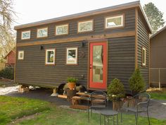 the tiny house is built on wheels and sits in front of a fenced yard