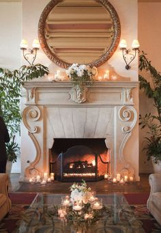 a living room with a fire place next to a mirror on the wall and candles in front of it