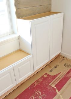 an unfinished kitchen with white cabinets and red rugs on the floor next to it