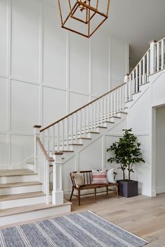 a white staircase with wooden handrails leading up to the second floor and a potted plant on the far side