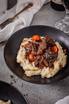 a black plate topped with mashed potatoes covered in beef and carrots next to a glass of wine