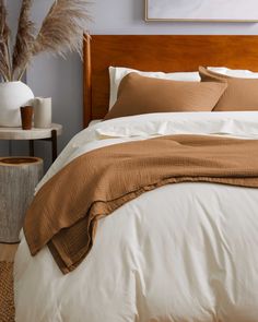 a bed with brown and white comforters in a bedroom next to a vase filled with dry grass