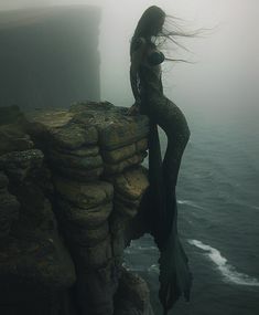 a woman with long hair standing on top of a cliff next to the ocean