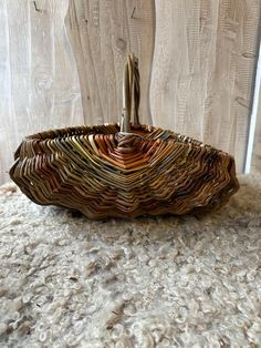 a woven basket sitting on top of a carpet next to a wooden fence with two sticks sticking out of it