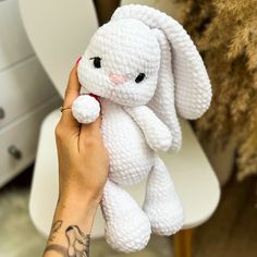 a hand holding a white crocheted bunny toy in front of a toilet seat