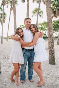 a man and two women hugging on the beach with palm trees in the back ground