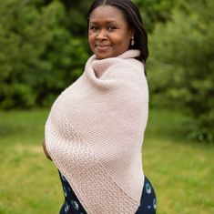 a woman wearing a pink knitted shawl in the grass with trees in the background