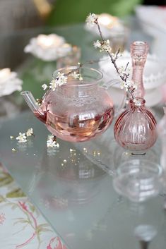 a glass tea pot with flowers in it on top of a table next to a vase