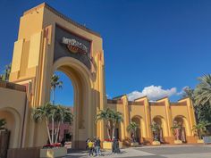 people are walking in front of the entrance to an amusement park with arches and palm trees