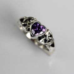 a silver ring with a purple stone in the middle and two hearts on each side