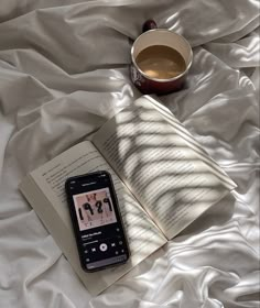 an open book, coffee cup and cell phone on a bed