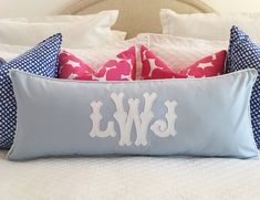 a bed with blue and white pillows, pink and white throw pillows, and a monogrammed pillow