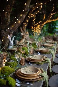 a long table with moss covered plates and place settings is set for an outdoor dinner