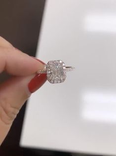 a woman's hand holding an engagement ring in front of a white box with a diamond on it