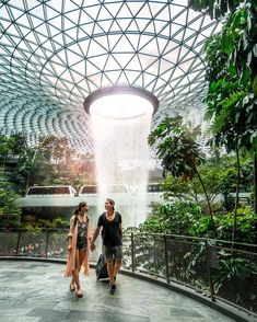 two people holding hands walking in front of a waterfall at the gardens by the bay