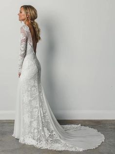 a woman in a white wedding dress standing against a wall with her back to the camera