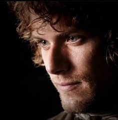 a close up of a man with curly hair and blue eyes looking at the camera