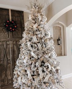 a white christmas tree with gold and silver ornaments on it in front of a wooden door