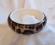 This is a fun vintage lucite bangle bracelet in an animal print design. The colors are black, brown and tan. The inside of the bracelet is white. The lucite is domed over the animal print giving the piece a nice dimensional appeal. It is in excellent vintage condition with virtually no sign of wear. It is one inch wide and has an inside wearable dimension of 2-5/8 inches. It is lightweight and easy to wear. Vintage Metal Bangle Bracelets, Bangle Bracelet, Eclectic Handmade Bangle Bracelets, Vintage Brass Bangle Bracelet, Vintage Cabochon Bangle Bracelets, Vintage Lucite Bangle Bracelet, Trio Halloween Costumes, Arm Bracelets, Vintage Bangles