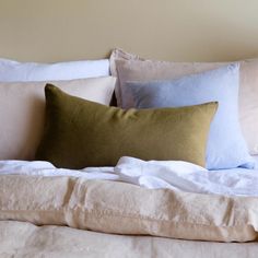 a bed topped with lots of pillows next to a white pillow case on top of a wooden headboard