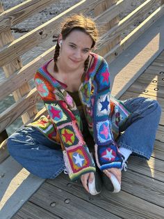 a woman sitting on the ground with her legs crossed wearing jeans and a colorful sweater