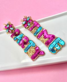 "The Beaded Party Time Earrings are the ultimate accessory for celebrating birthdays, girls' nights, bachelorette parties, graduations or just to celebrate the end of the week! These fabulous earrings are designed to make a statement, featuring bold pink and blue lettering that spells out \"Party Time\" to ensure you're ready to have a blast and make memories that last a lifetime. Crafted with attention to detail, our Party Time Earrings showcase high-quality materials and impeccable craftsmansh Fun Dangle Earrings For Party, Pink Fun Jewelry For Party, Adjustable Fun Party Earrings, Party Earrings For Mother's Day, Fun Pink Party Jewelry, Multicolor Jewelry For Valentine's Day Party, Pink Fun Party Jewelry, Mother's Day Party Jewelry With Matching Earrings, Mother's Day Party Jewelry Set With Earrings