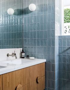 a bathroom with two sinks and blue tiles on the shower wall, along with a wooden cabinet