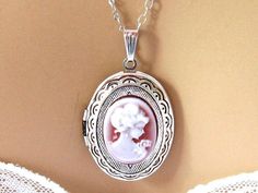 "Romantic Victorian cameo locket necklace with a pendant of a neoclassical woman and flowers against a burgundy red cameo background. The cameo is set in a light weight oval silver plated locket decorated with outer etchings, and you have your choice of a shiny silver finish (shown), gunmetal, and antiqued silver. Also available in gold or bronze. The open locket can hold 2 pictures, and hangs on a rhodium (white gold) plated chain. Length: 18 inches, Locket Pendant: 1.5 inches Please leave a no Elegant Locket Necklace For Wedding, Charming Silver Necklace For Wedding, Elegant Vintage Charm Locket Necklace For Formal Occasions, Elegant Formal Locket Necklace With Vintage Charm, Elegant Locket Necklace With Vintage Charm For Formal Occasions, Elegant Silver Locket Necklace, Charming Pendant Necklace For Wedding, Elegant Pink Jewelry With Engraving, Elegant Pink Locket Jewelry