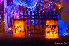 halloween decorations and lights decorate the front yard of a house with an iron gate that says you dare