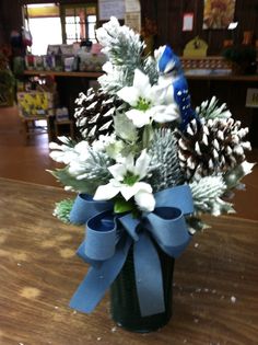 a vase filled with white flowers and pine cones on top of a wooden table in a store