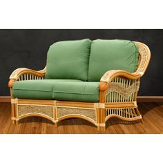 a wicker chair with green cushions on top of wooden floor next to black wall