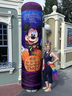 a woman standing next to a sign for mickey mouse's halloween party