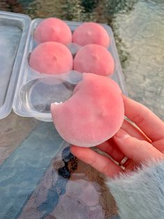 a person holding some pink donuts in front of two trays of ice cream