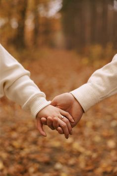 two people holding hands while walking through leaves