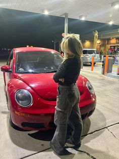 a woman standing next to a red car