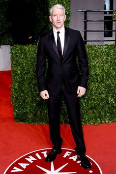 a man in a black suit and tie standing on a red carpet at an event