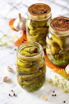 three jars filled with pickles sitting on top of a table next to garlic and mushrooms