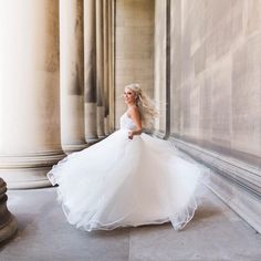 a woman in a white wedding dress is walking down the street with her hair blowing in the wind