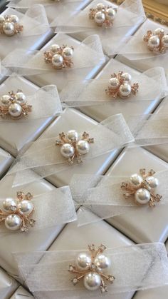 several pairs of pearl and crystal brooches are on display in white boxes with bows