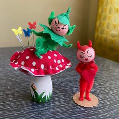 two small dolls are standing on top of a mushroom