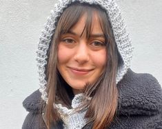 a woman wearing a gray and white knitted hoodie with a cat ears on it