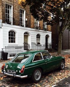 an old green car parked on the side of the road in front of a building