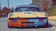 an orange and blue sports car parked on the side of the road with trees in the background