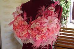 a mannequin with pink flowers and feathers on it's neck, sitting in front of a window